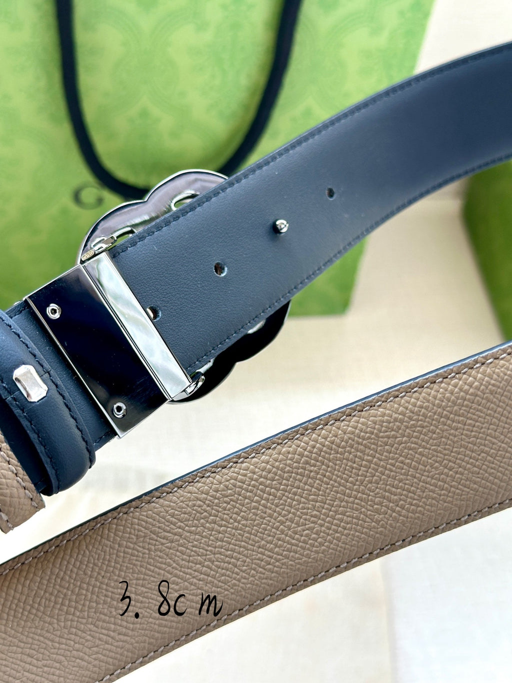 Gucci belt buckle close-up on beige leather strap with dark blue lining and silver G