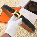 Black leather belt with gold-tone buckle and tan underside, stitched edges and keeper tab