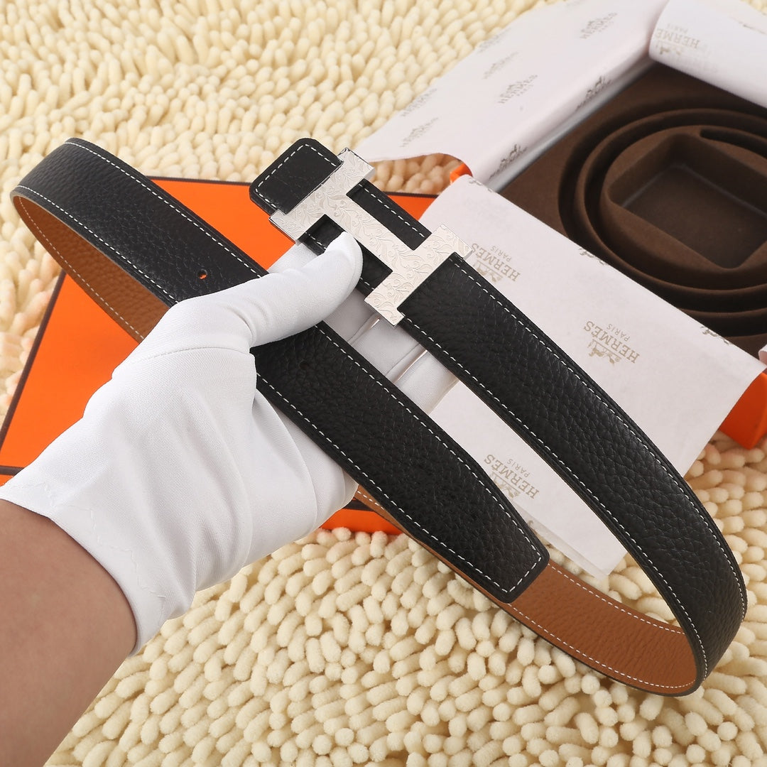 Black leather belt with large gold-tone H buckle, contrast stitching, and tan keeper strap