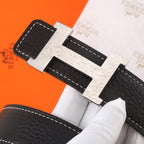 Black leather belt with silver-toned buckle, ornate texture, and white contrast stitching