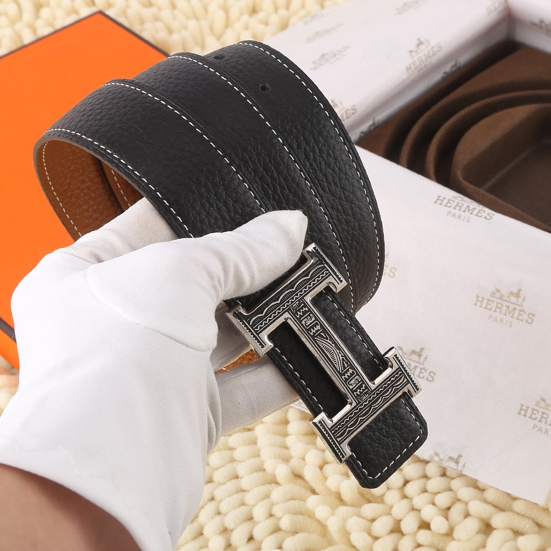 Black leather belt with silver engraved buckle, held by white-gloved hand