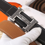 Black leather belt close-up of silver buckle with decorative engraving and stitching