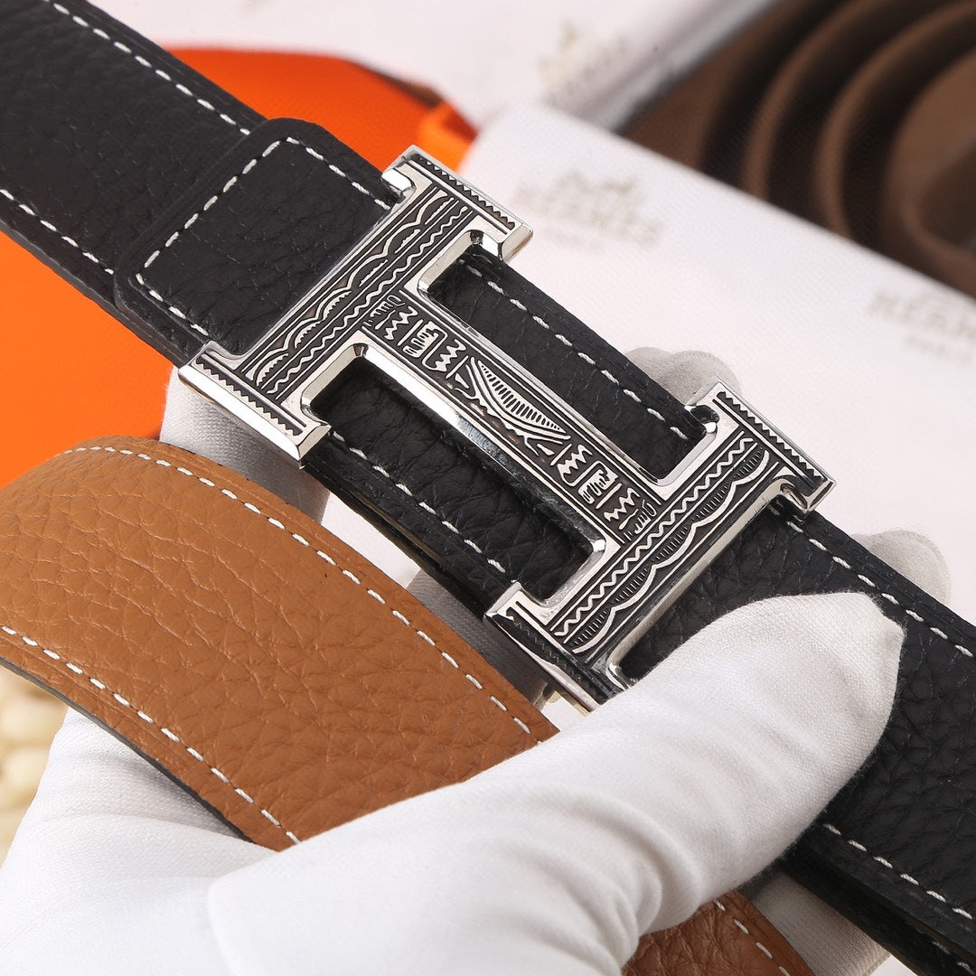 Black leather belt close-up of silver buckle with decorative engraving and stitching