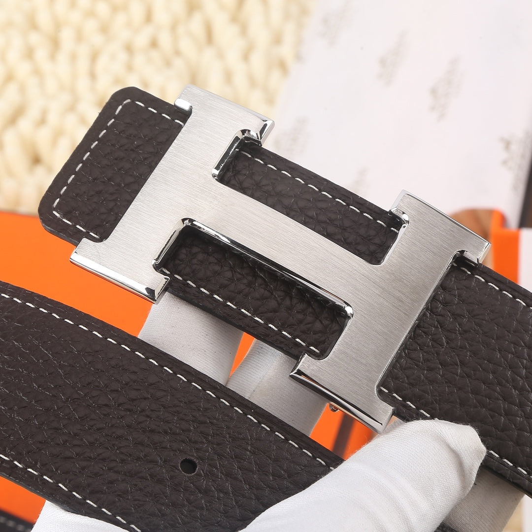 Dark leather belt closeup of gold-tone buckle hardware with white contrast stitching.