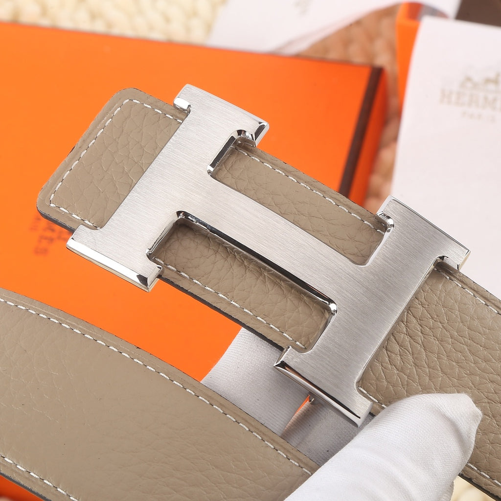 Hermes belt buckle close-up: gold H clasp on taupe leather strap.