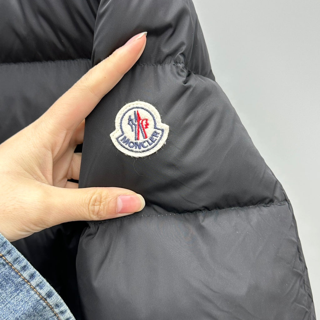 Dark puffer jacket logo patch on chest area; close-up with hand
