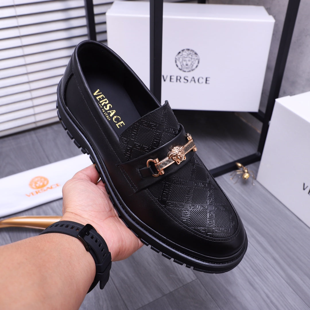 Versace luxury black loafers on hand, gold buckle detail on textured vamp