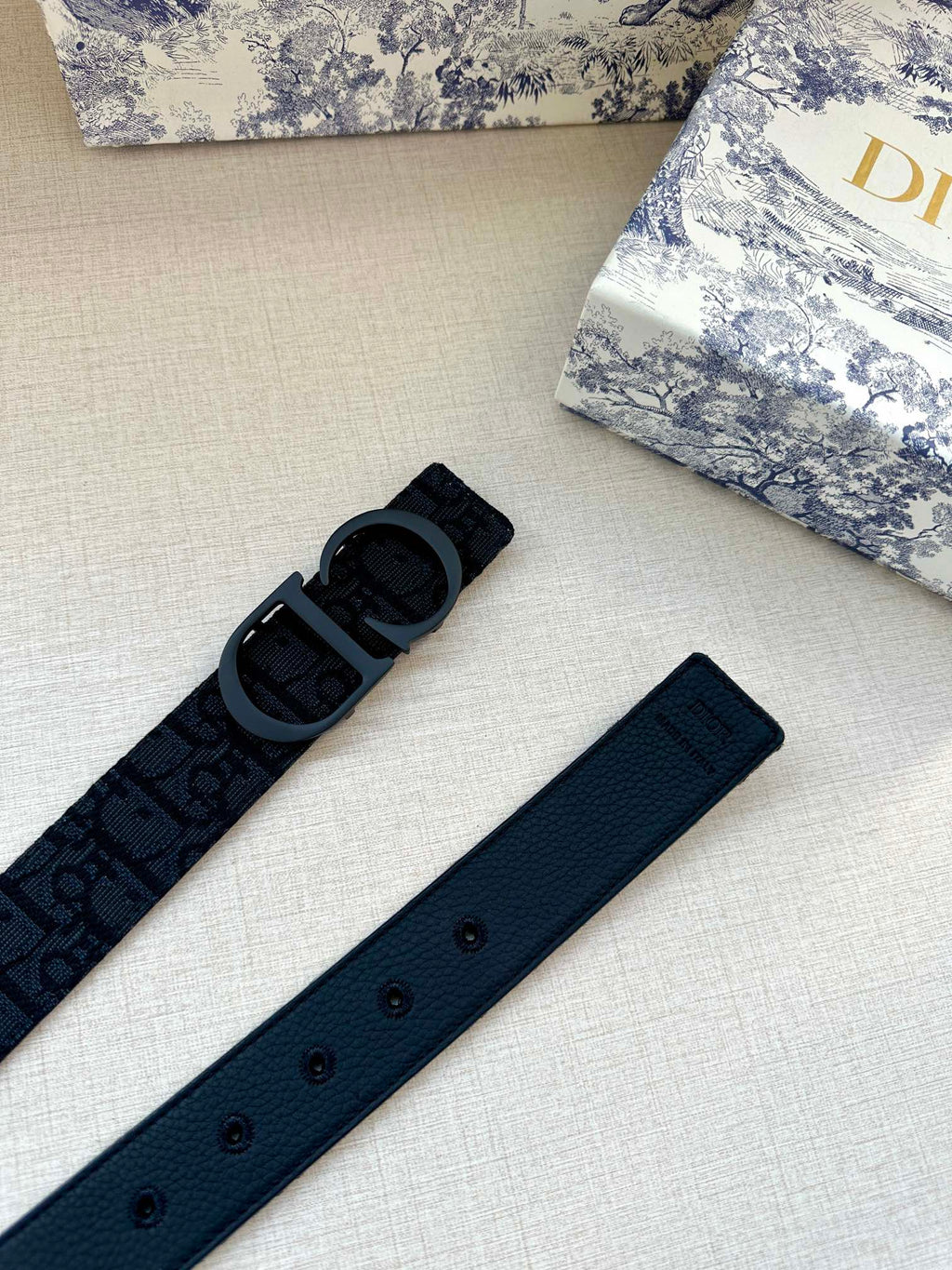 Dark blue fabric belt with repeating logo pattern and multiple adjustment holes