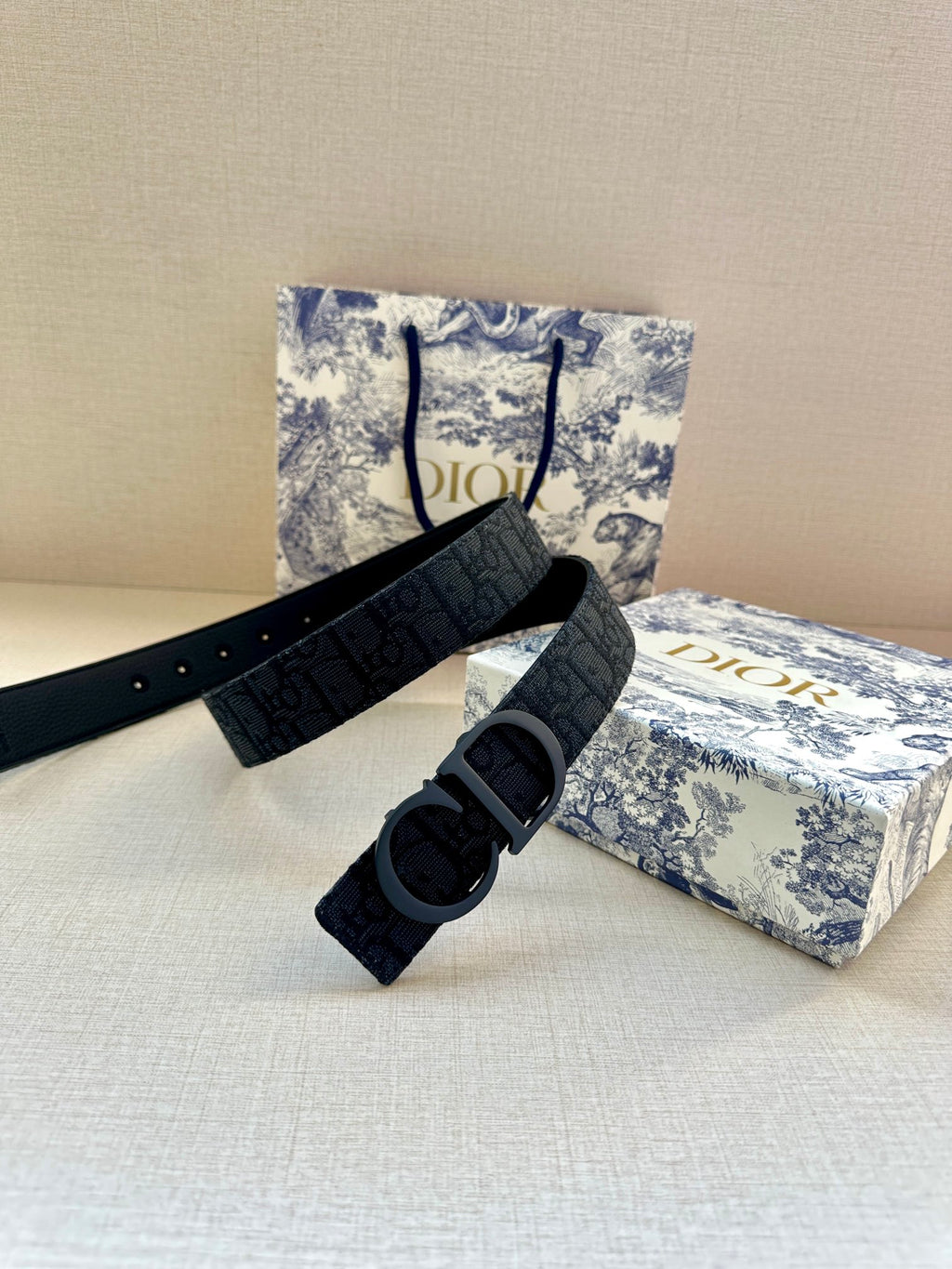 Dark blue designer belt with large buckle and logo pattern, shown in an open loop