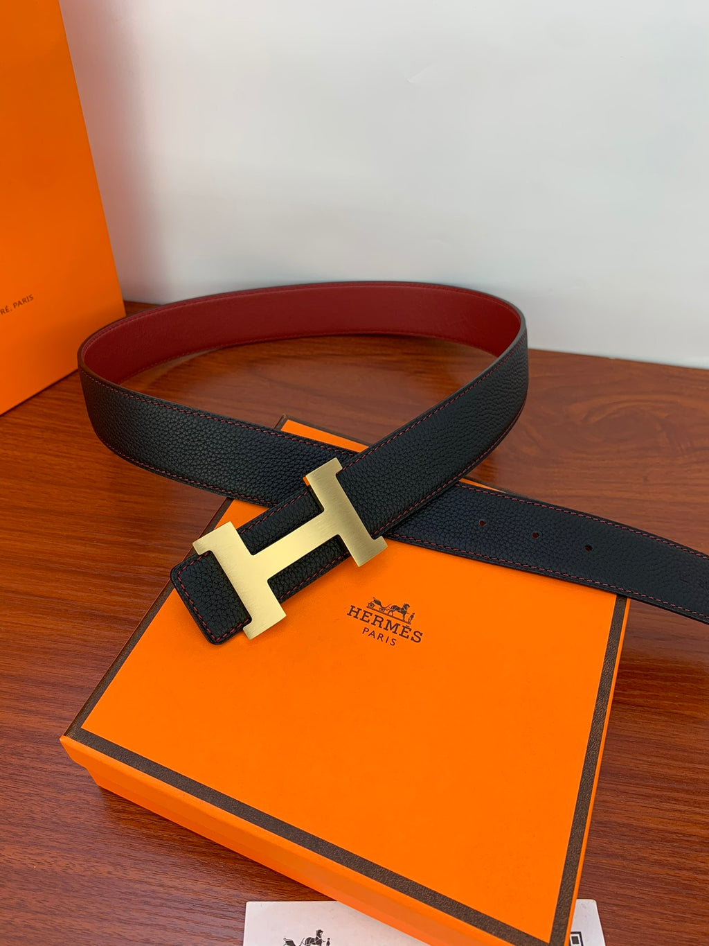 Black leather belt with gold-tone H buckle laid on orange box