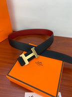 Black leather belt with gold-tone H buckle laid on orange box