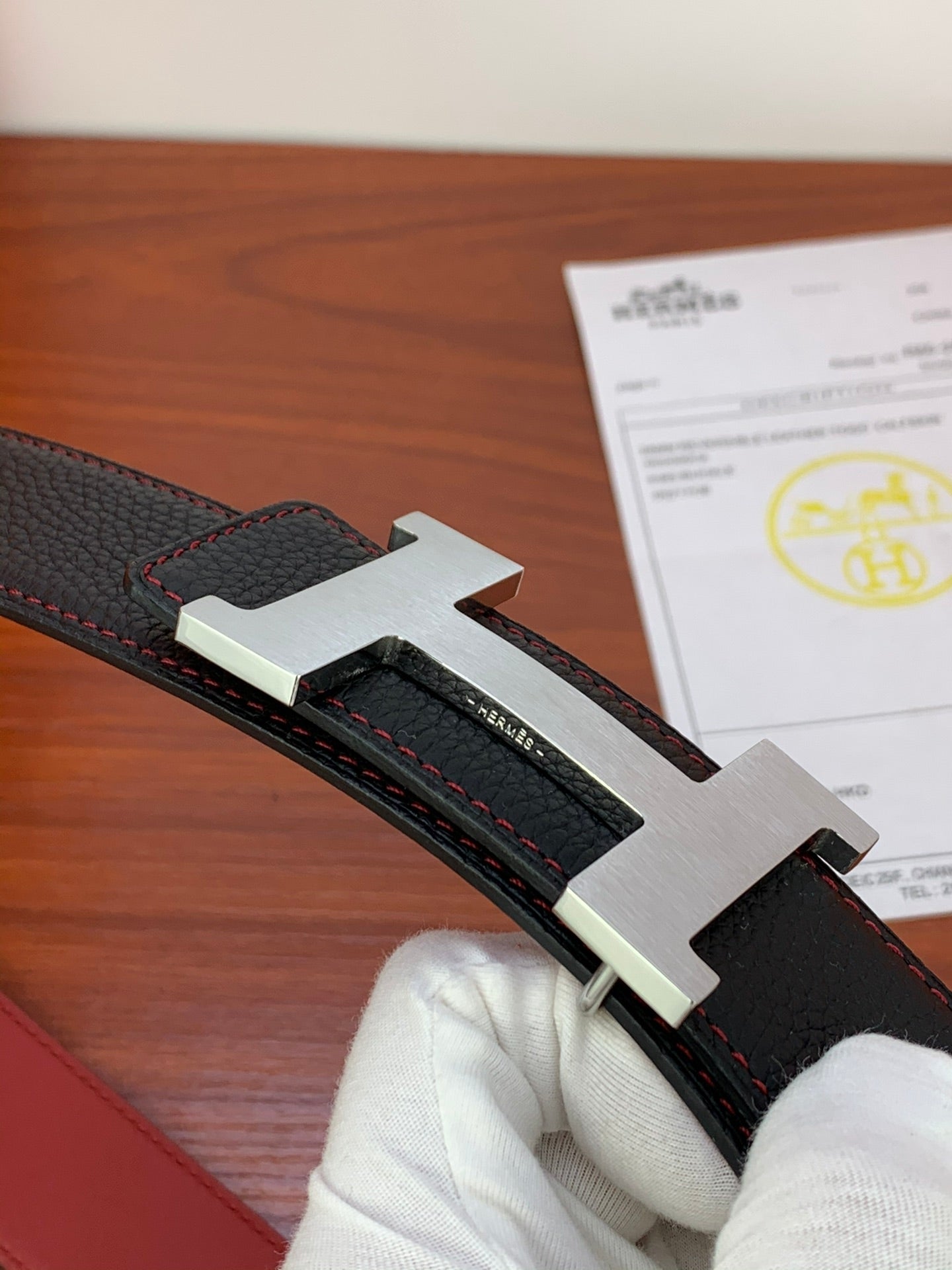 Black leather belt detail with silver-tone buckle and red-stitch keeper