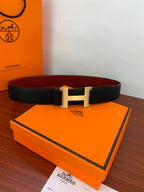 Black leather belt with gold-tone H buckle on orange box and card