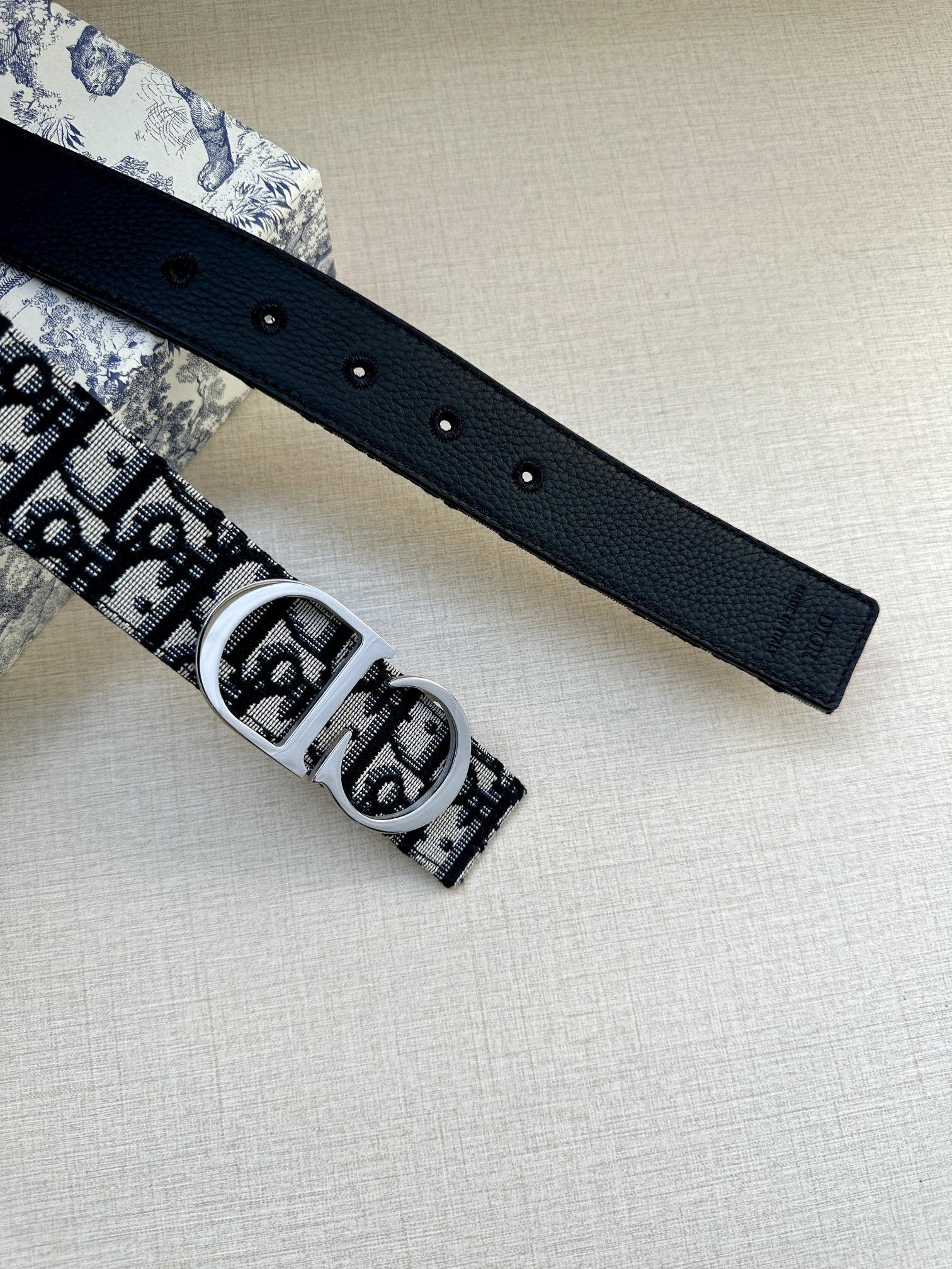 Dior belt flat lay with textured dark strap, silver buckle, and punched holes