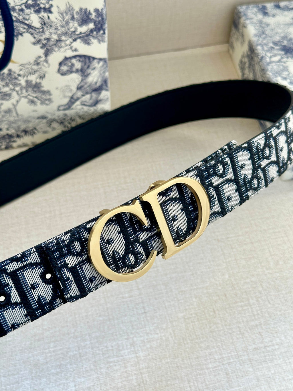 Dior belt close-up: navy-and-white logo jacquard strap with gold CD buckle