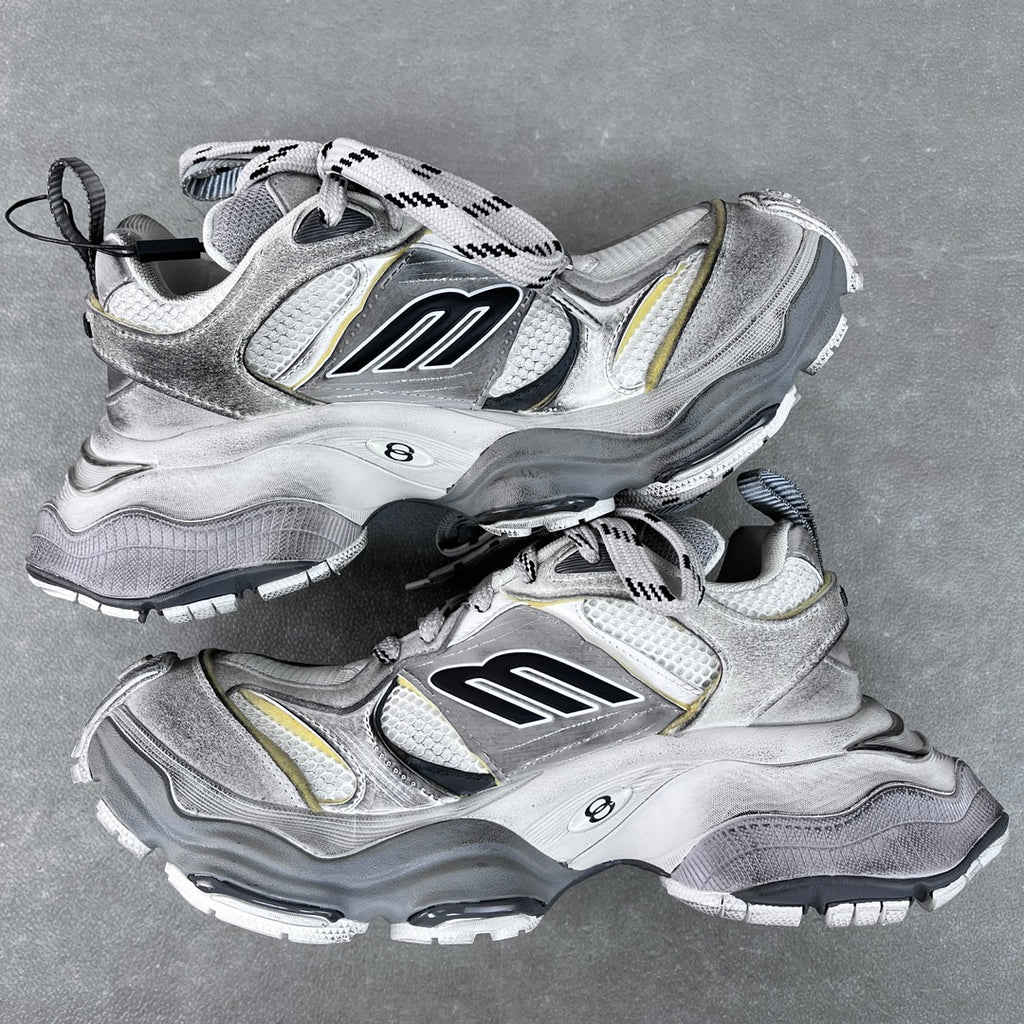 Balenciaga unisex sneakers angled view, silver with black logo panels and yellow detailing.