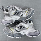 Balenciaga unisex sneakers angled view, silver with black logo panels and yellow detailing.