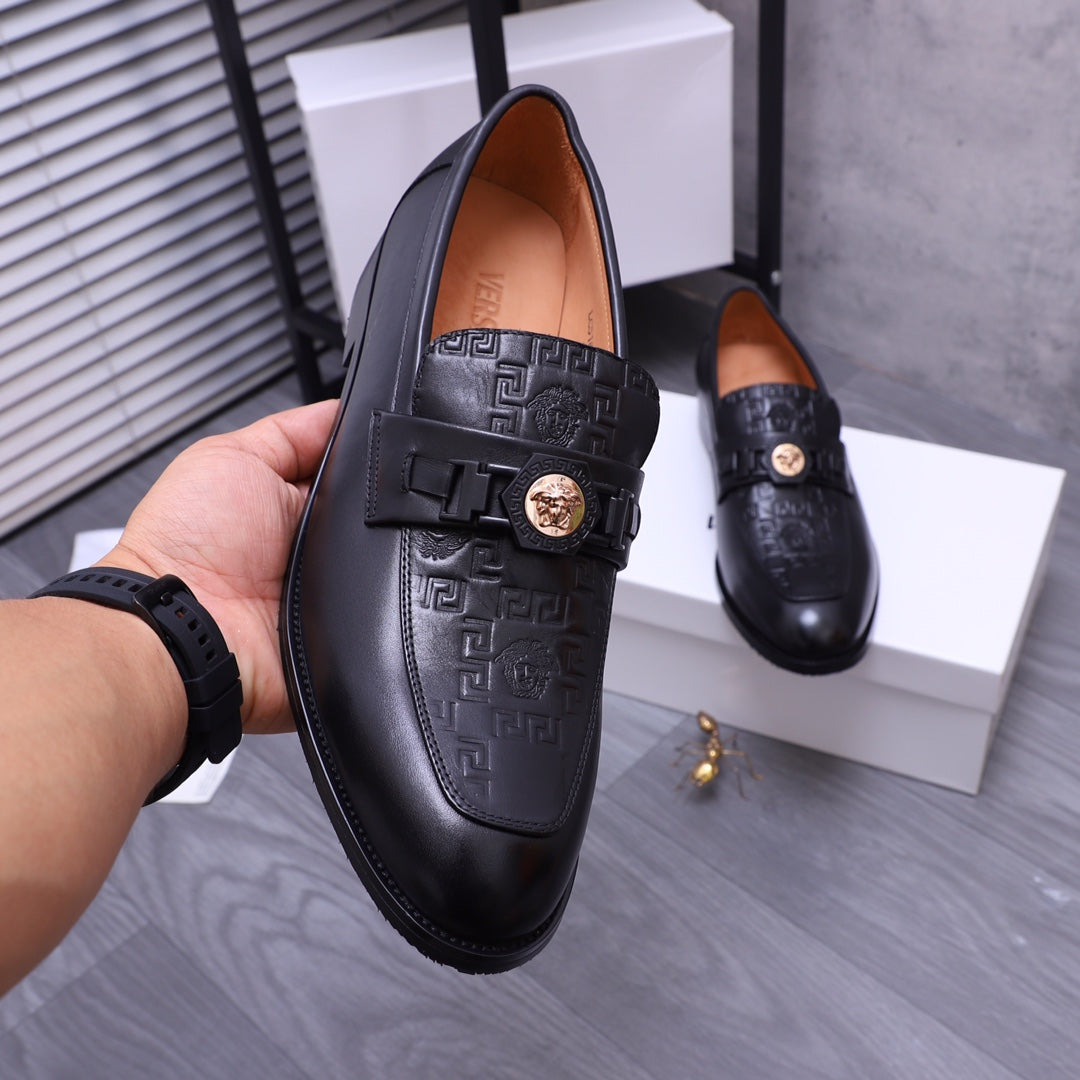 Close-up of black Versace loafers with embossed pattern and gold crest buckle