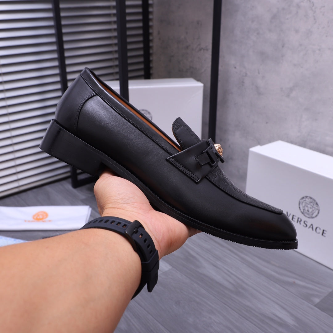 Black Versace loafer held in hand with strap and gold crest on upper
