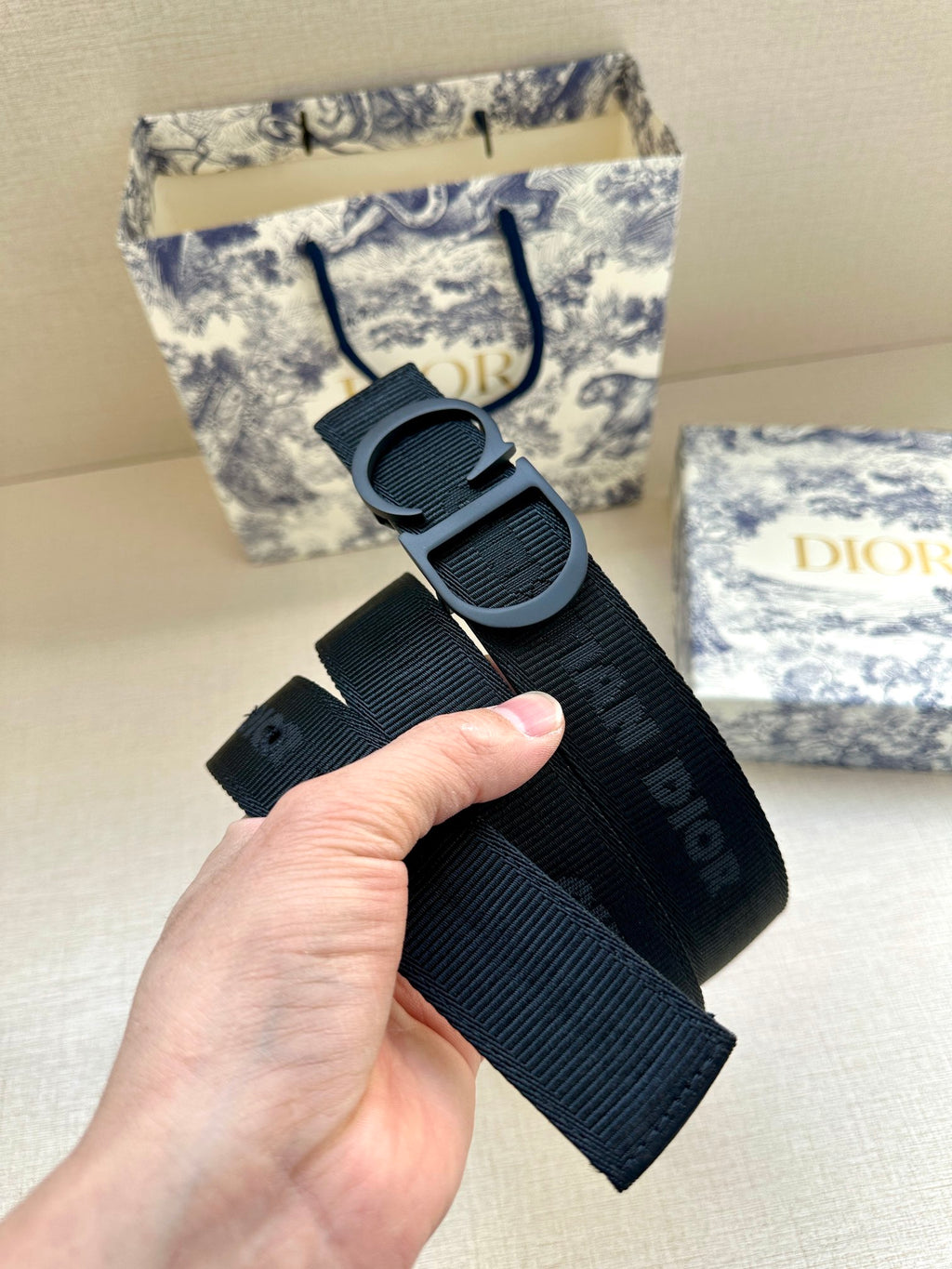 Black Dior belt held in hand, showing large CD buckle and strap holes.