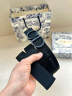 Black Dior belt held in hand, showing large CD buckle and strap holes.