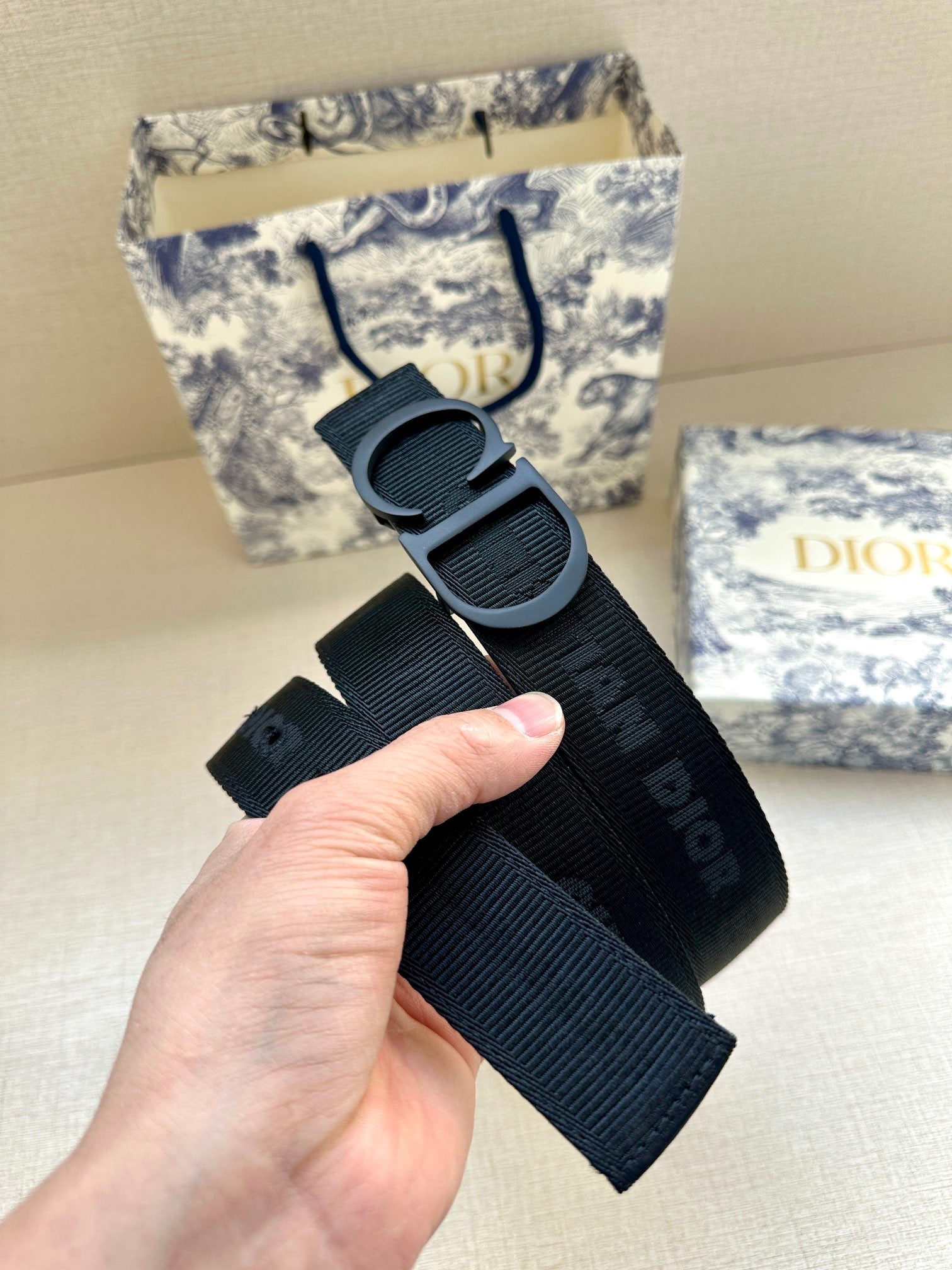 Black Dior belt held in hand, showing large CD buckle and strap holes.