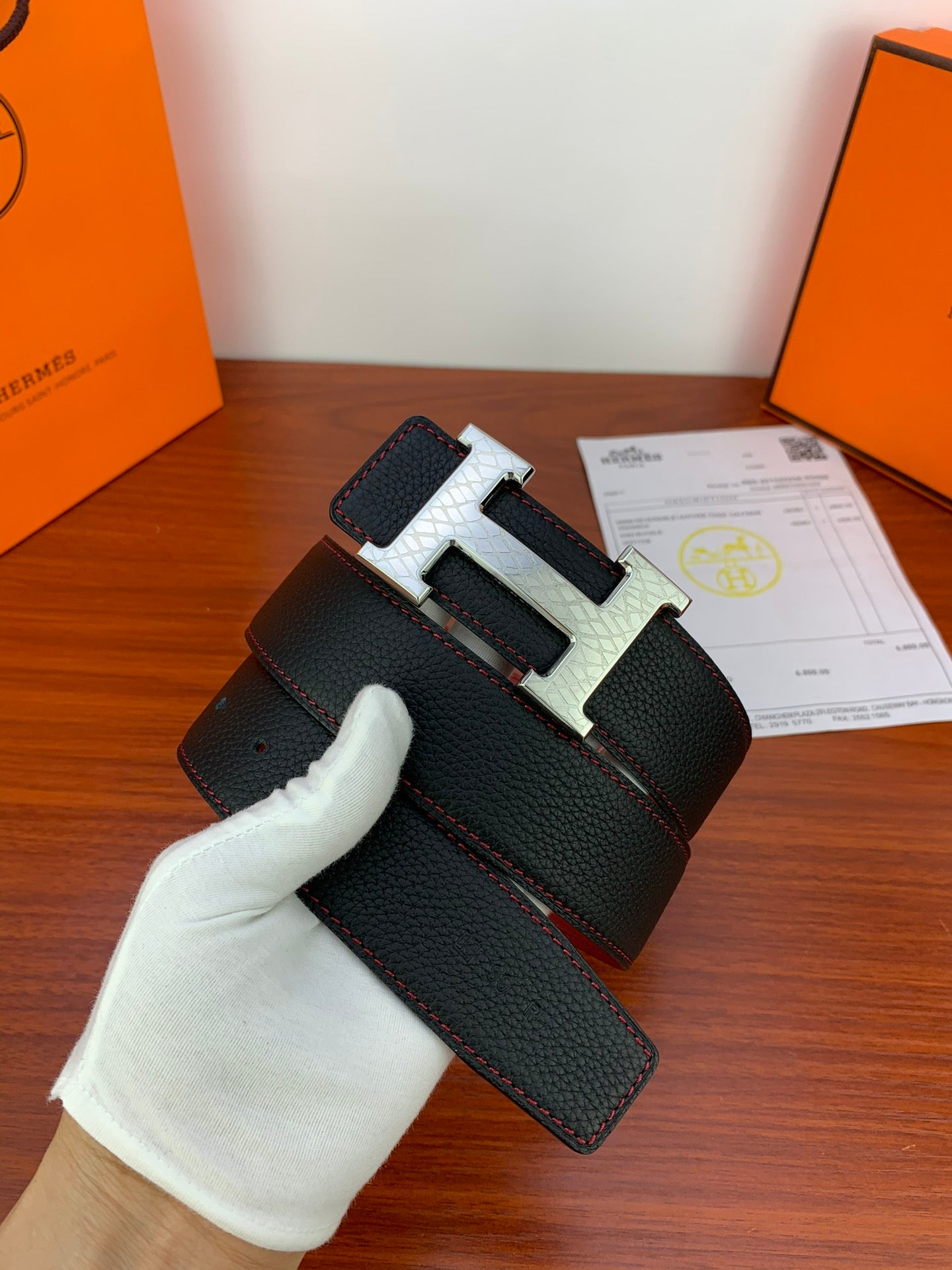Black textured leather belt with silver-toned H buckle, shown on display