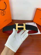 Black leather belt with wide silver H buckle, textured strap held by white glove