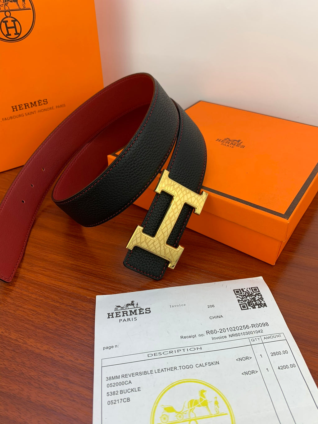 Black leather belt with gold H buckle and maroon underside, side view