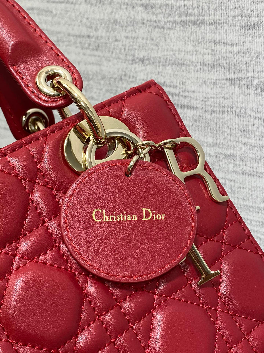 Round leather charm tag reading Christian Dior on red quilted Dior bag