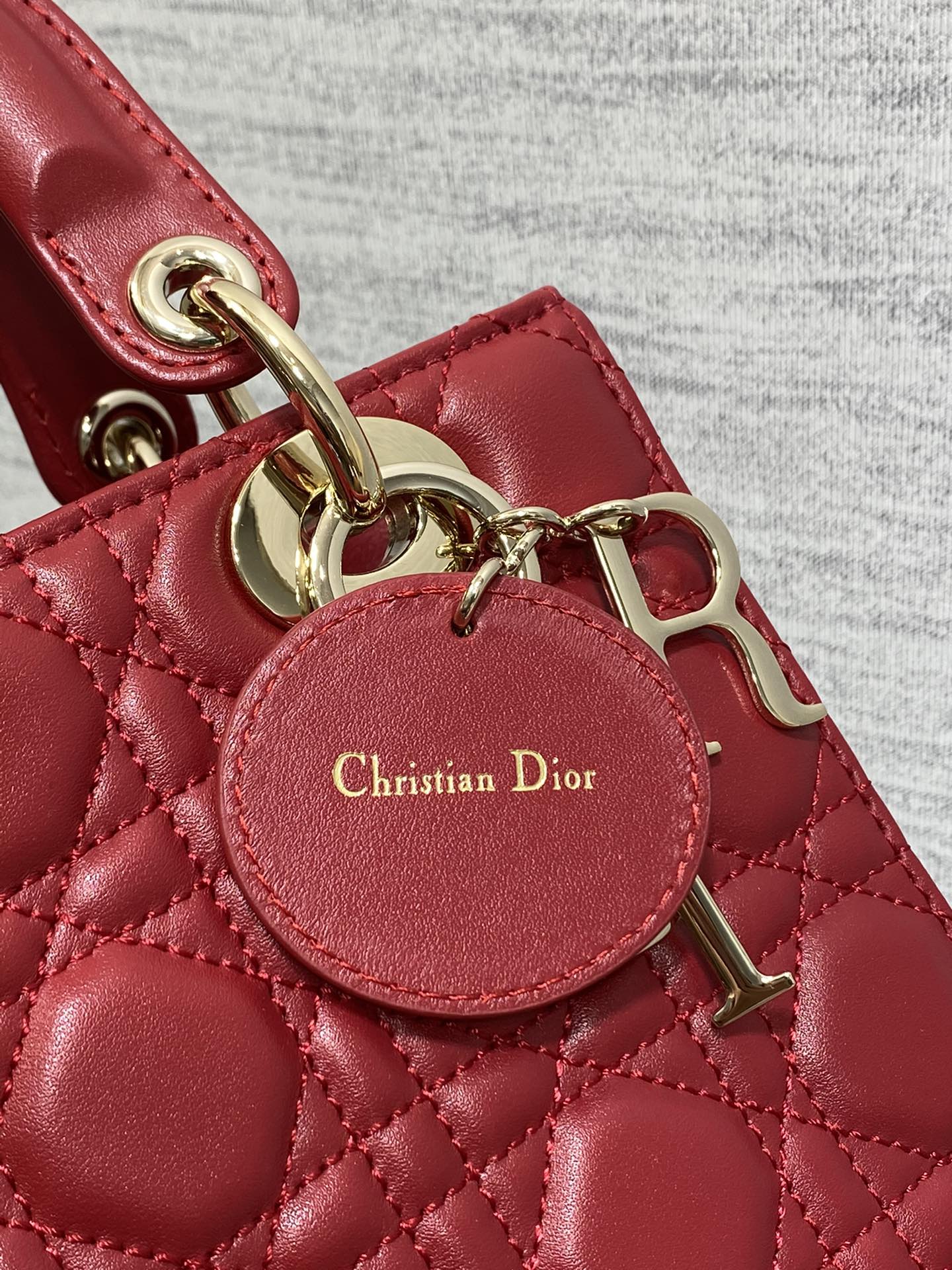 Round leather charm tag reading Christian Dior on red quilted Dior bag