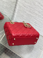 Red quilted Dior handbag with top handle, gold logo plate, and metal feet
