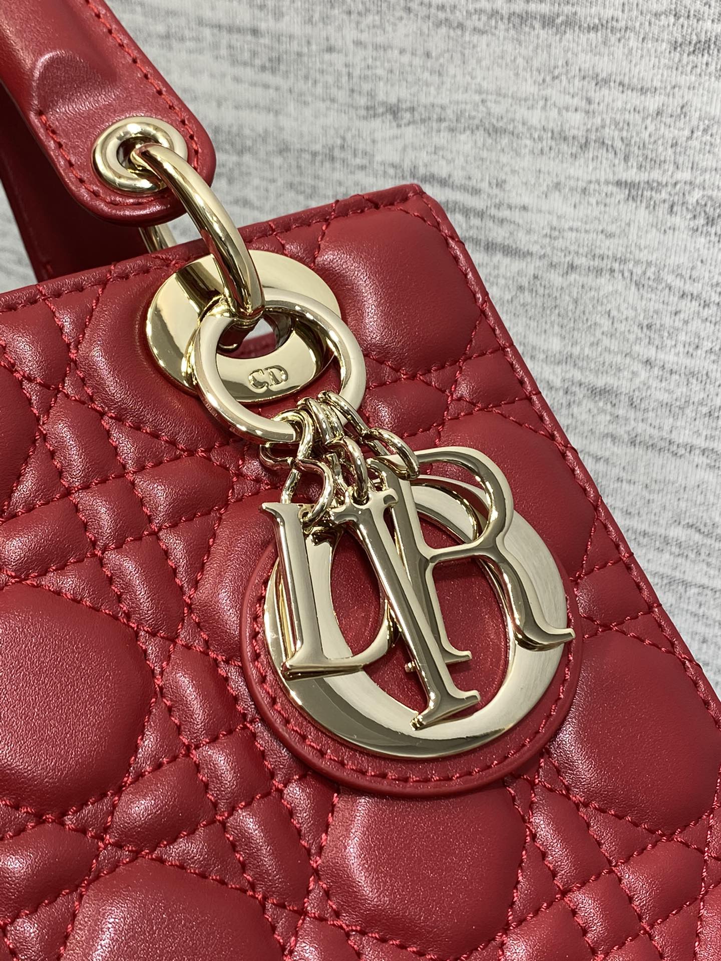 Gold logo charm on red quilted Dior handbag handle hardware