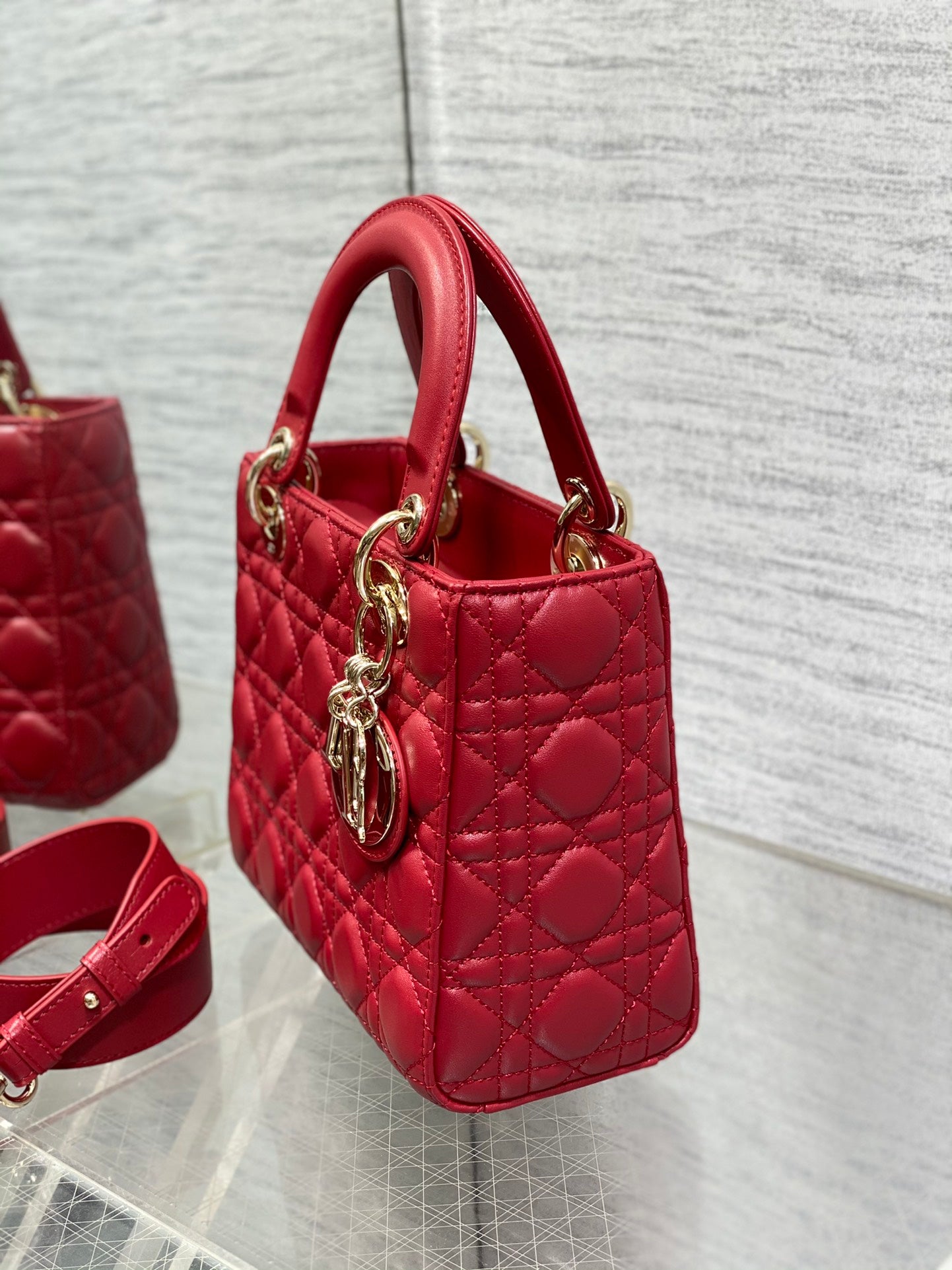 Red quilted Dior handbag side view with top handles, gold rings, logo charm