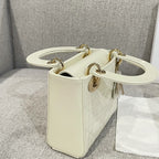 Cream Dior handbag with top handles, gold rings, and leather-like front