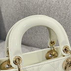 Cream patent-style top handle with gold clasp rings on quilted Dior handbag