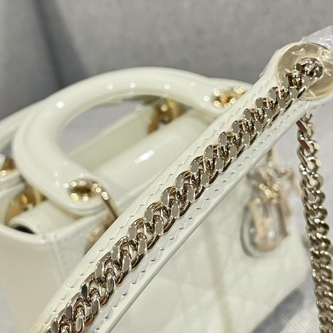 Gold chain strap on cream Dior handbag with glossy handle and hardware
