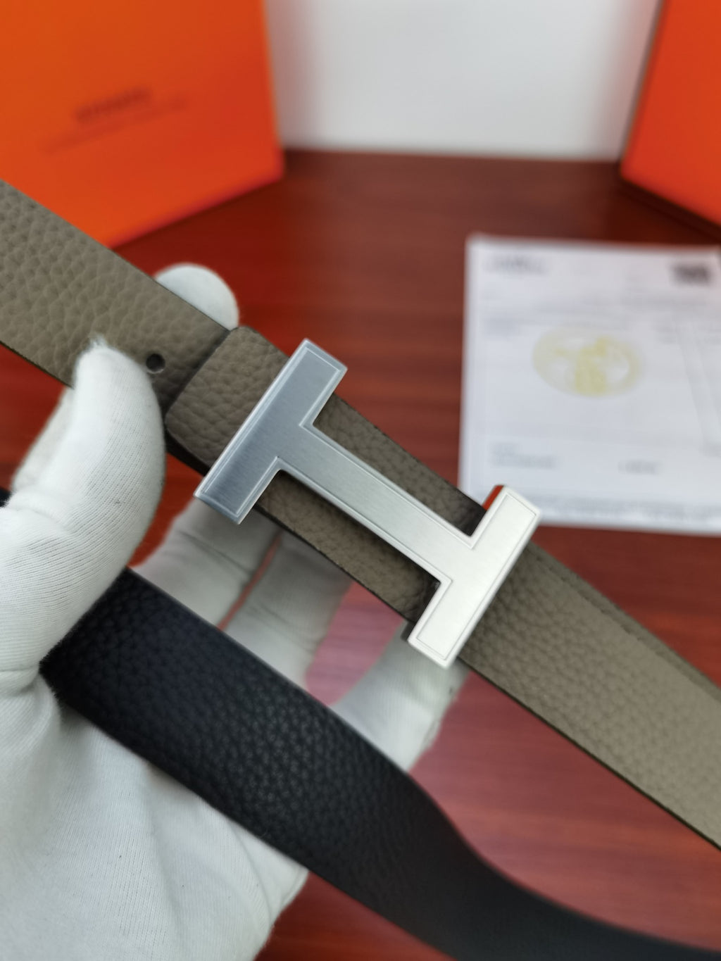 Reversible leather belt, close-up of silver-tone buckle on light gray strap