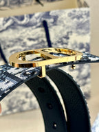 Gold buckle on black belt with subtle monogram print, close-up detail