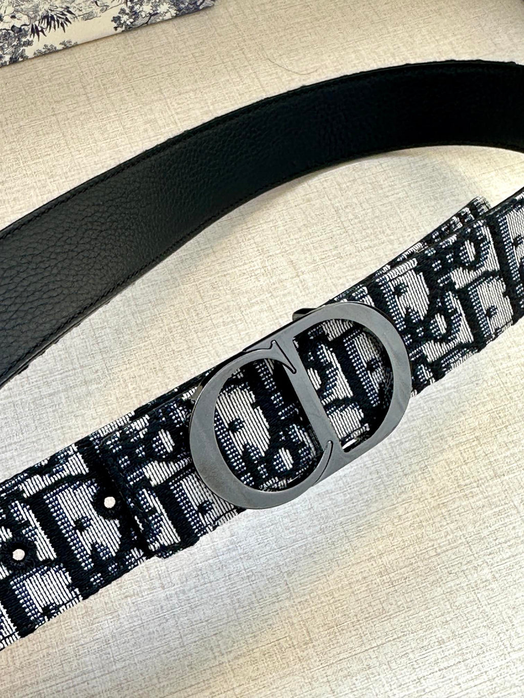 Black patterned belt strap with large round silver-tone buckle detail