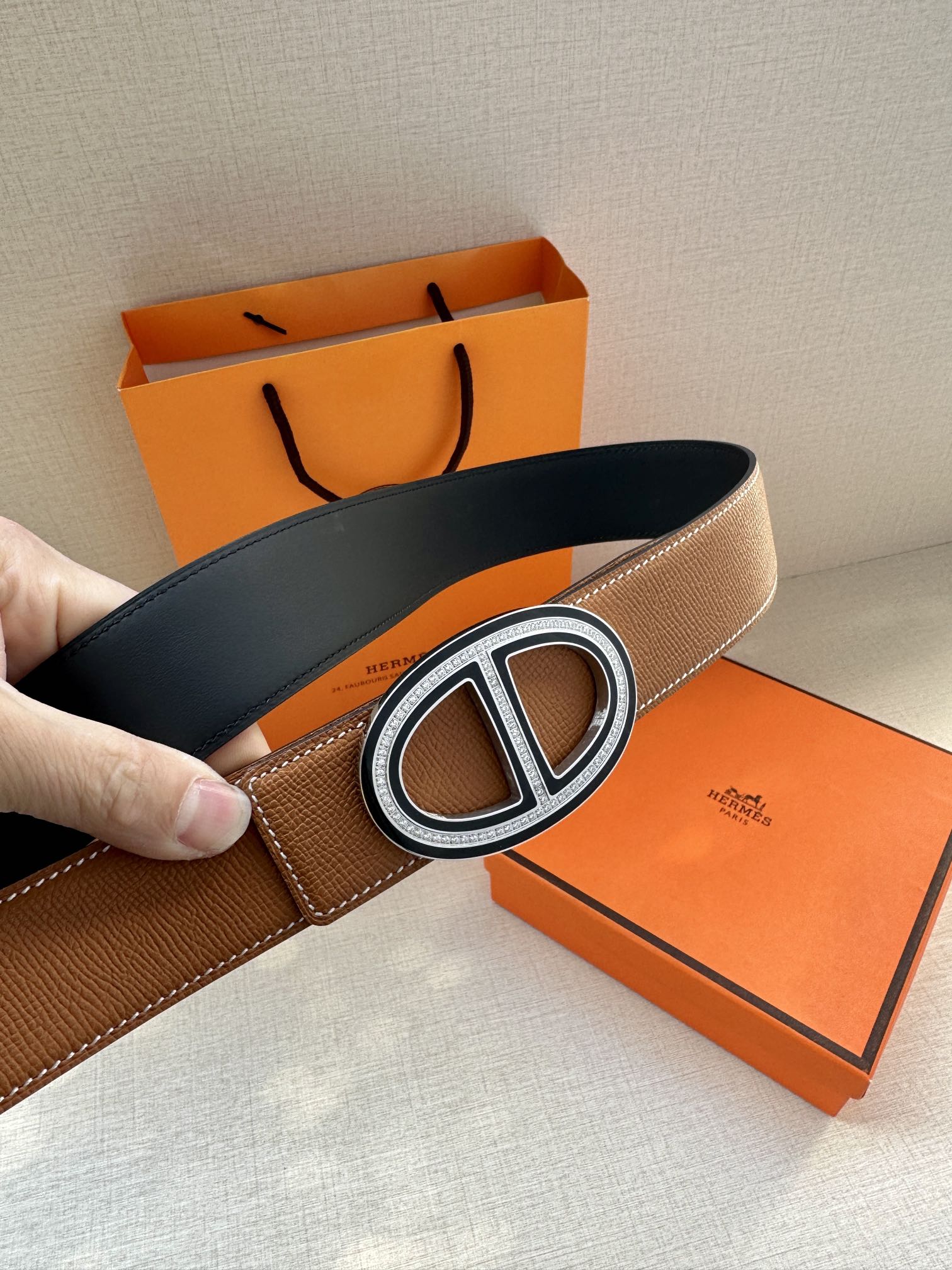 Tan leather belt with O-shaped silver buckle and visible black underside