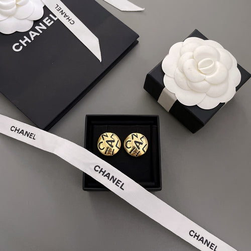 Gold CHANEL logo stud earrings with interlocking letters on a white ribbon card
