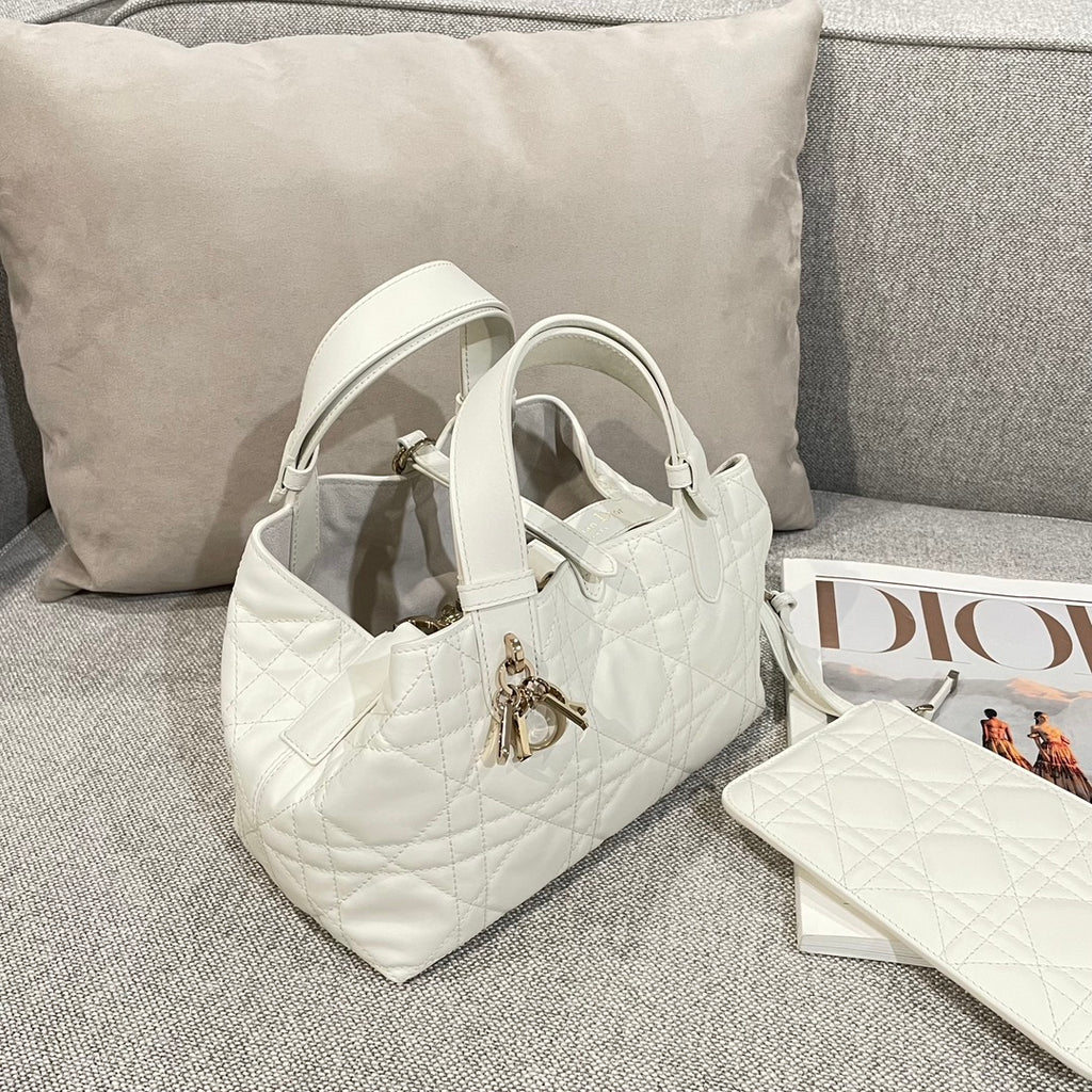 Quilted white handbag with top handles and gold logo charm, angled view
