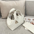 Quilted white handbag with top handles and gold logo charm, angled view