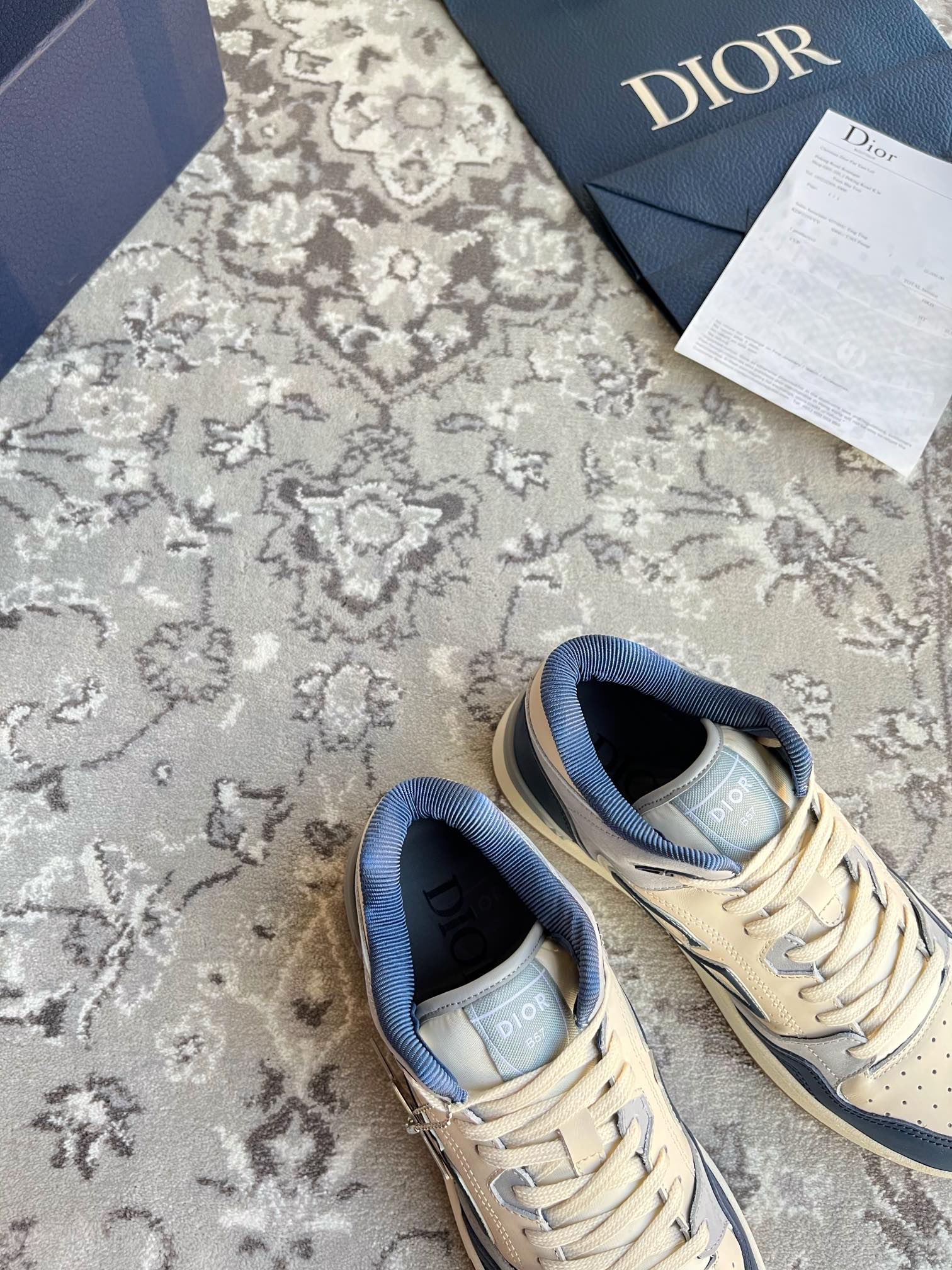 Pair of Dior unisex lace-up sneakers, cream and navy, CD logo on quarter panels.