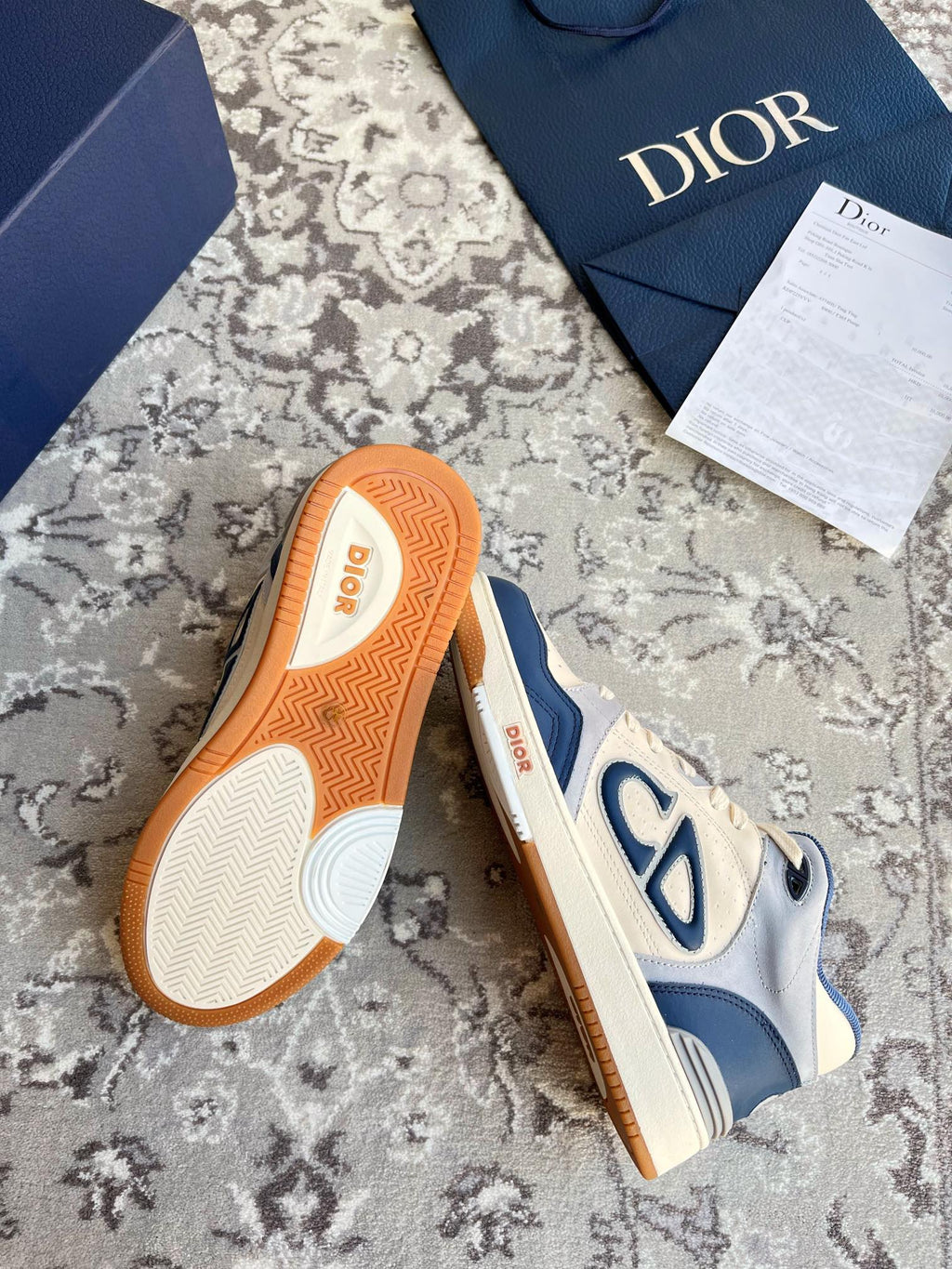 Dior unisex sneakers showing orange tread soles on cream and navy upper.