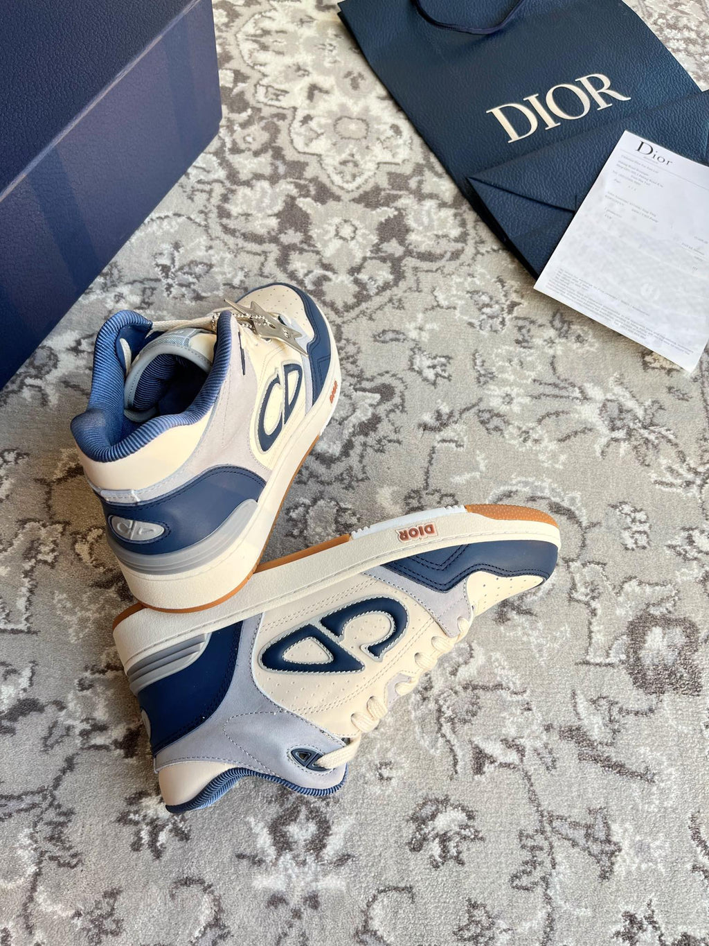 Dior unisex sneakers shown from heel and side, cream and navy with orange outsole.