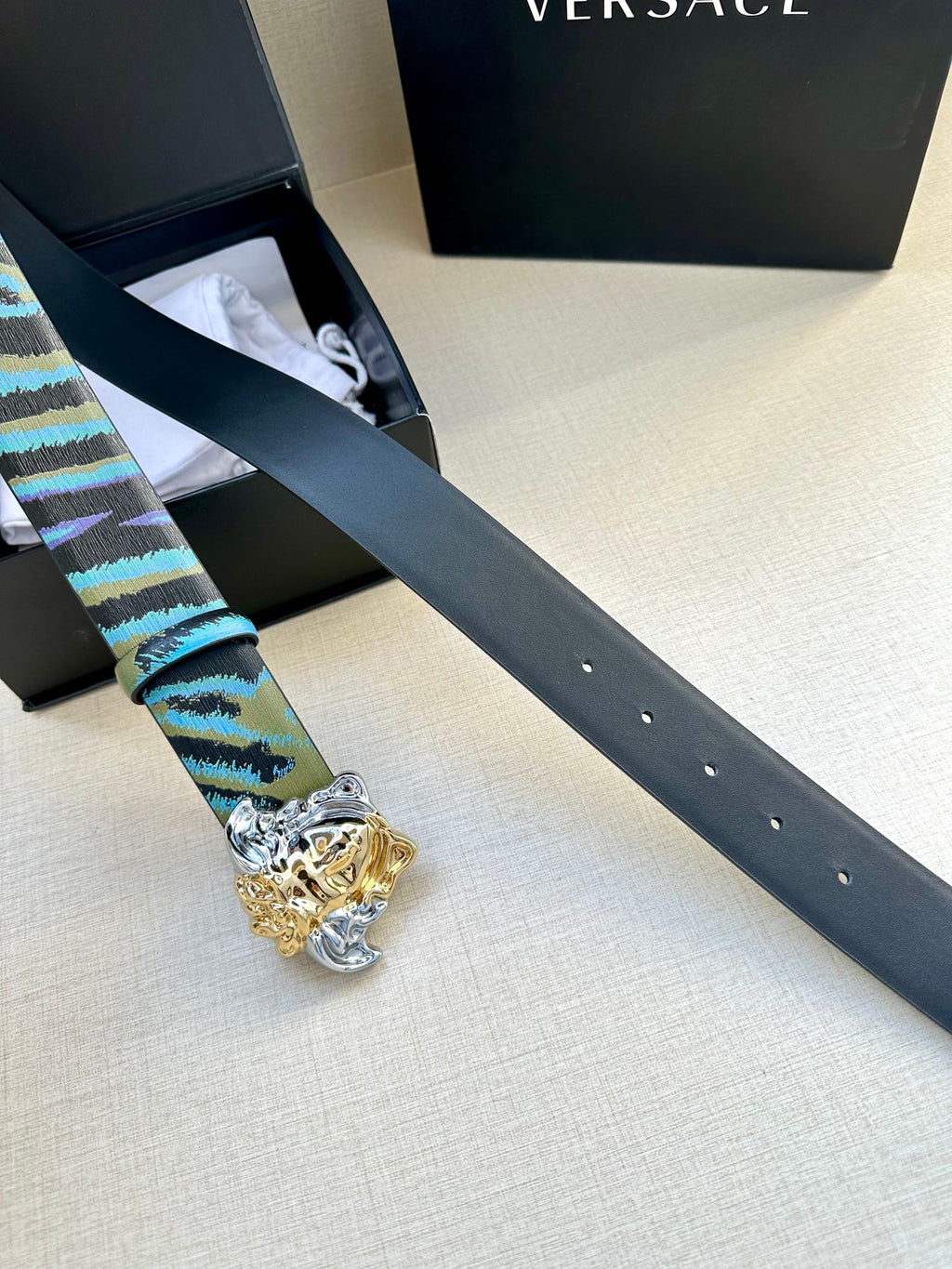 Versace belt laid out: blue and teal striped strap with gold Medusa buckle and silver details