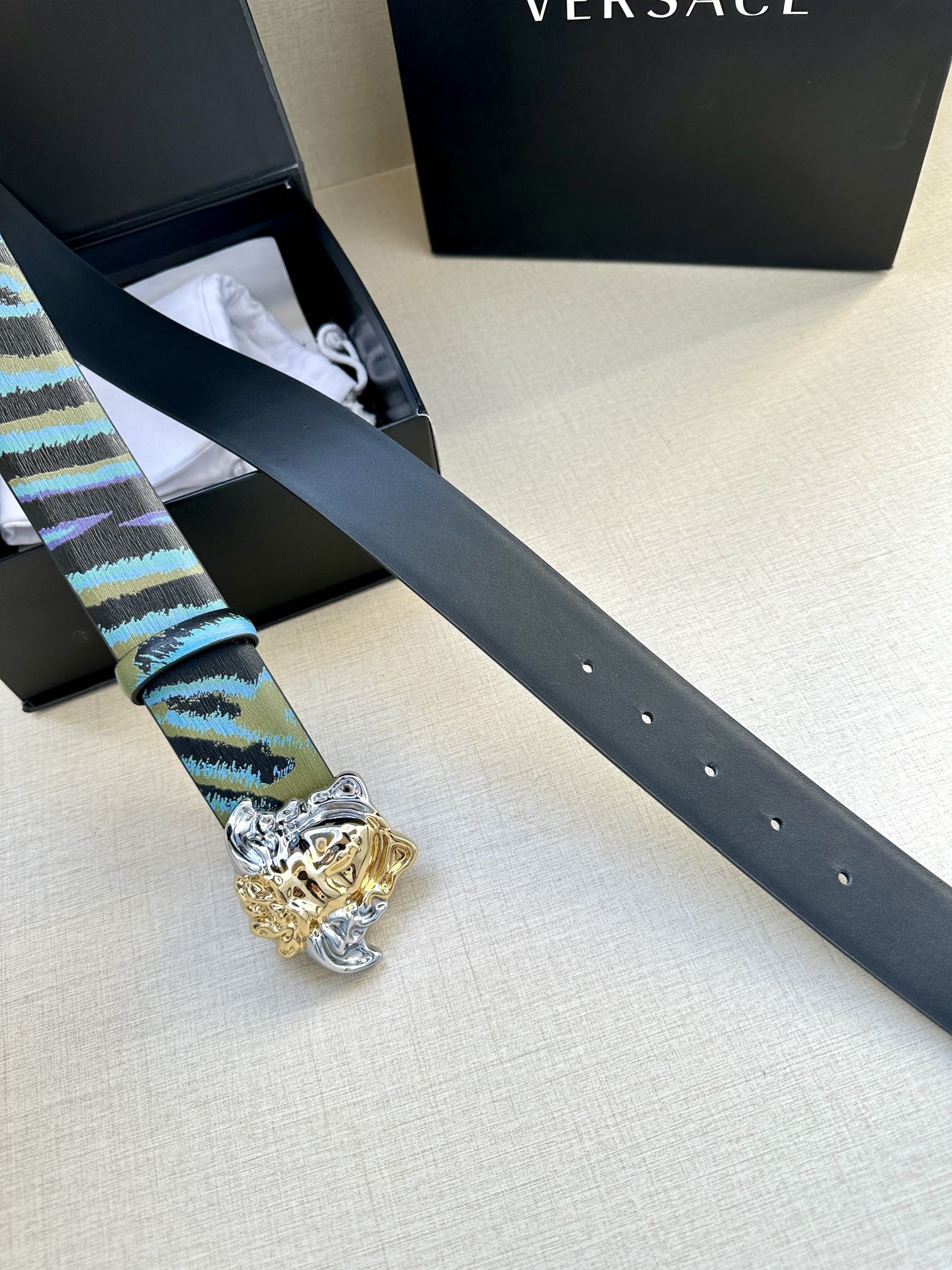 Versace belt laid out: blue and teal striped strap with gold Medusa buckle and silver details
