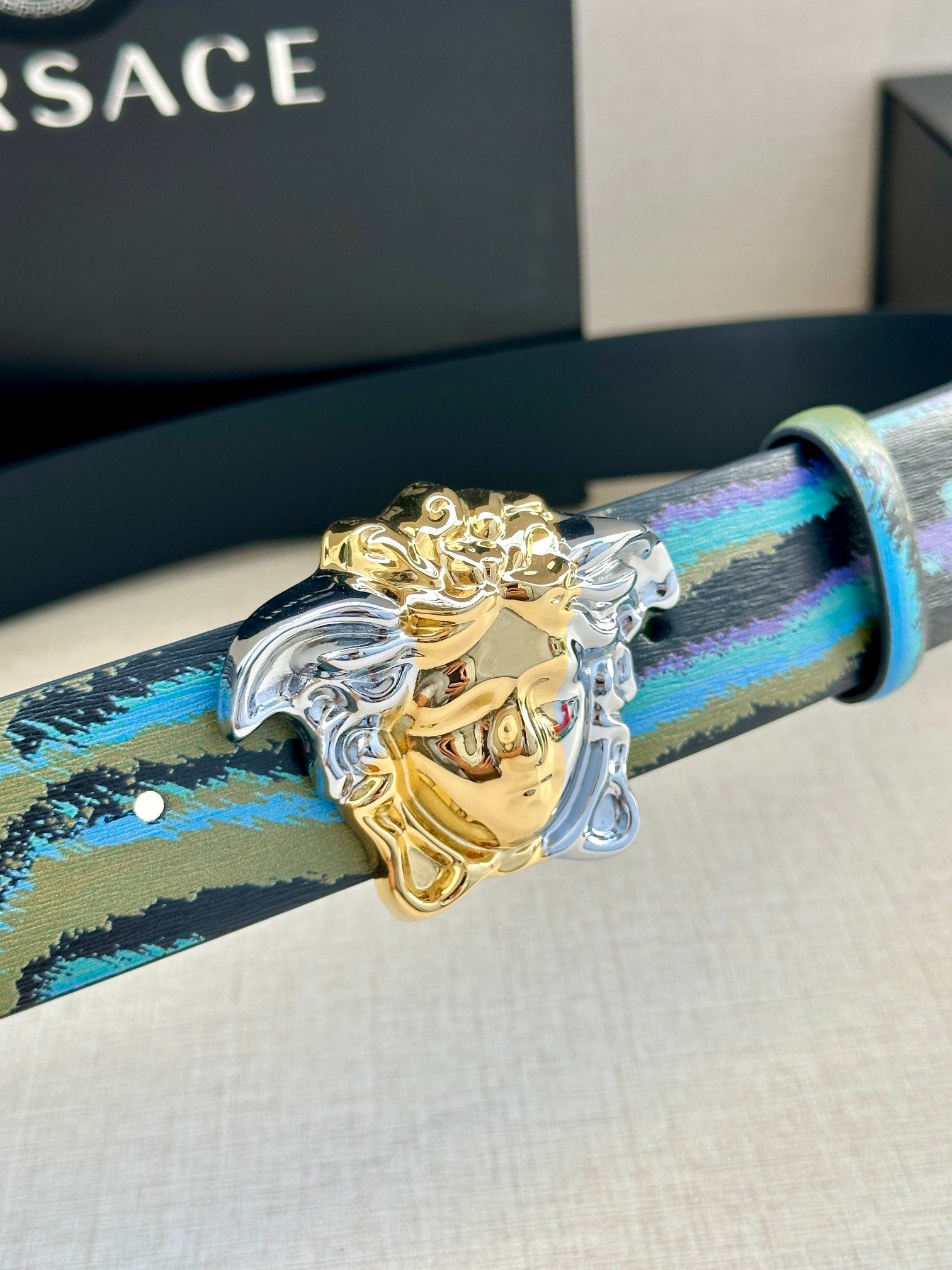 Versace belt close-up: blue and teal striped strap with gold Medusa buckle and silver hardware